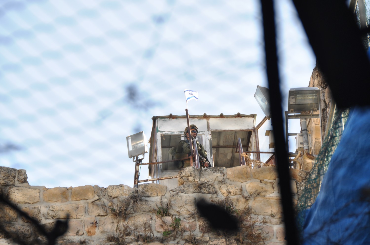 A soldier overlooking Hebron; seen through the nets